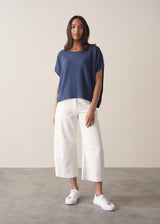 Woman wearing a navy blue sleeveless sweater and white barrel leg jeans and trainers