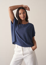 Woman wearing a navy blue sleeveless sweater and white barrel leg jeans