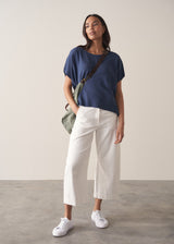 Woman wearing a navy blue sleeveless sweater and white barrel leg jeans and trainers