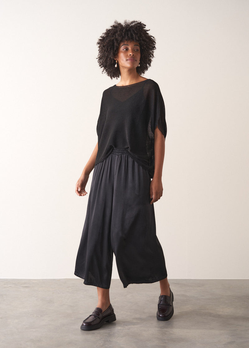 Woman wearing a black sheer sparkle top against a plain background