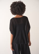 Woman wearing a black sheer sparkle top against a plain background