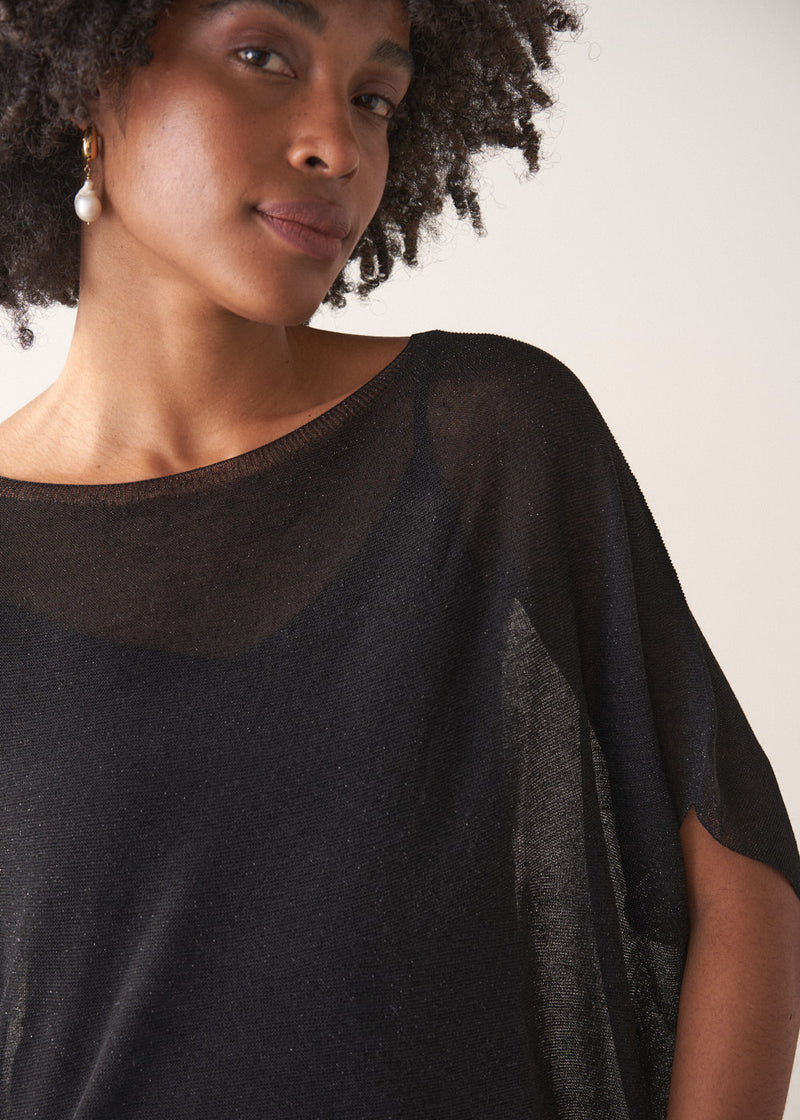 Woman wearing a black sheer sparkle top against a plain background