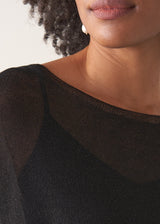 Woman wearing a black sheer sparkle top against a plain background