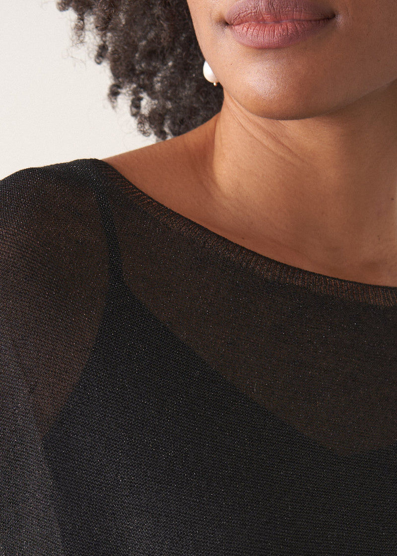 Woman wearing a black sheer sparkle top against a plain background