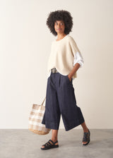 Woman wearing cream light knit sweater and blue denim jeans against a plain background.