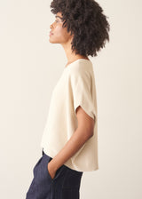 Woman wearing cream light knit sweater and blue denim jeans against a plain background.