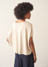 Woman wearing cream light knit sweater and blue denim jeans against a plain background.