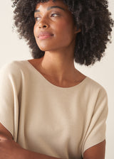 Woman wearing cream light knit sweater and blue denim jeans against a plain background.
