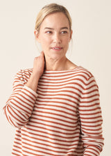 Woman wearing burnt orange and oatmeal striped fine knit sweater with blue denim trousers