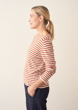Woman wearing burnt orange and oatmeal striped fine knit sweater with blue denim trousers