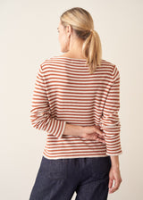 Woman wearing burnt orange and oatmeal striped fine knit sweater with blue denim trousers