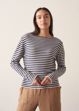 Woman wearing dark grey and off white stripe knit sweater and brown linen trousers