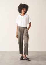 Woman wearing a white linen short sleeve shirt and khaki green satin cargo trousers against a plain background