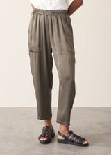 Woman wearing a white linen short sleeve shirt and khaki green satin cargo trousers against a plain background