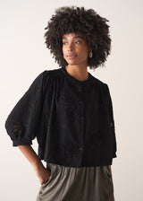 Woman wearing a black vintage-style jacquard blouse with khaki satin trousers on a neutral background