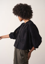 Woman wearing a black vintage-style jacquard blouse with khaki satin trousers on a neutral background