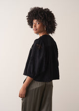 Woman wearing a black vintage-style jacquard blouse with khaki satin trousers on a neutral background