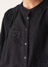 Woman wearing a black vintage-style jacquard blouse with khaki satin trousers on a neutral background