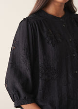 Woman wearing a three-quarter sleeve black devore jacquard top with dark blue satin trousers against a plain background