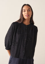 Woman wearing a three-quarter sleeve black devore jacquard top with dark blue satin trousers against a plain background
