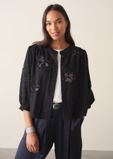 Woman wearing a three-quarter sleeve black devore jacquard top with dark blue satin trousers against a plain background