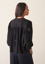 Woman wearing a three-quarter sleeve black devore jacquard top with dark blue satin trousers against a plain background