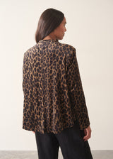 A woman wearing a matching leopard-print jacket and trousers set with a white shirt and a black clutch bag.