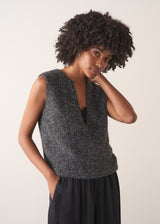 Woman wearing a grey sleeveless sparkle knit sweater and black wide leg satin trousers against a plain background