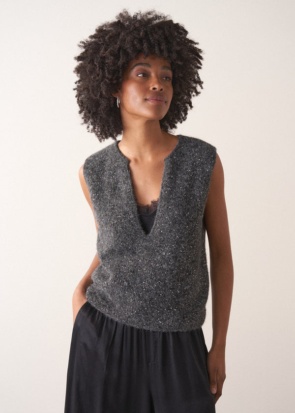 Woman wearing a grey sleeveless sparkle knit sweater and black wide leg satin trousers against a plain background