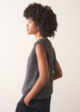 Woman wearing a grey sleeveless sparkle knit sweater and black wide leg satin trousers against a plain background