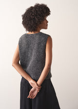 Woman wearing a grey sleeveless sparkle knit sweater and black wide leg satin trousers against a plain background