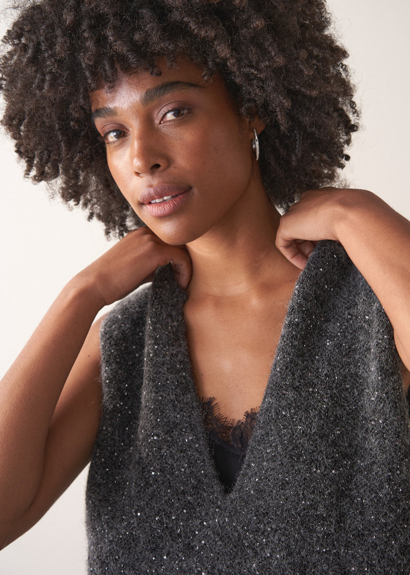 Woman wearing a grey sleeveless sparkle knit sweater and black wide leg satin trousers against a plain background