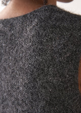 Woman wearing a grey sleeveless sparkle knit sweater and black wide leg satin trousers against a plain background