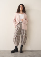 Woman wearing an oversized blush pink chunky knit cardigan with checked trousers and black boots