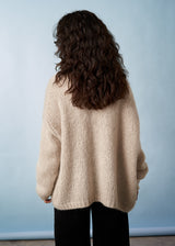 Woman wearing a soft oatmeal chunky cardigan facing a neutral background