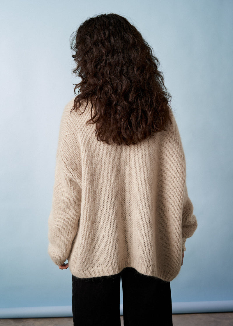 Woman wearing a soft oatmeal chunky cardigan facing a neutral background
