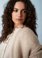 Close up of woman wearing a soft oatmeal chunky cardigan over a white shirt.