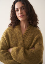 Woman wearing an olive green chunky knitted cardigan against a plain background