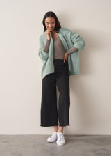 Woman wearing a mint green chunky knit cardigan with a striped top and black wide leg trousers