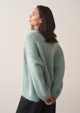 Woman wearing a mint green chunky knit cardigan with a striped top and black wide leg trousers