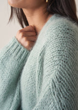 Woman wearing a mint green chunky knit cardigan with a striped top and black wide leg trousers