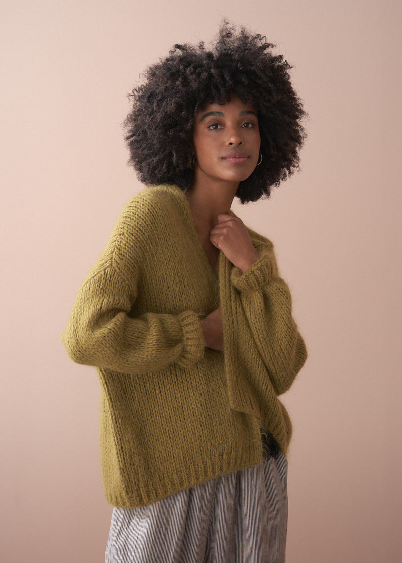 Woman wearing an olive green chunky knit cardigan with striped trousers