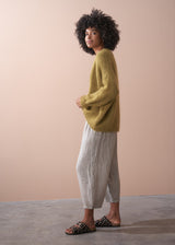 Woman side on, wearing an olive green chunky knit cardigan with striped ankle length trousers with a neutral background