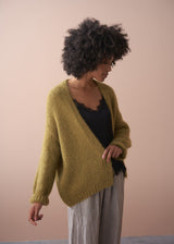 Woman wearing a chunky knit olive cardigan, black satin cami and striped trousers on neutral background