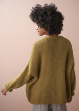 Woman wearing a chunky knit olive green chunky cardigan, facing a neutral background
