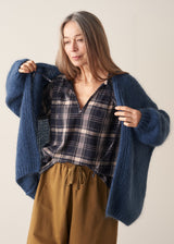 A woman wearing a blue chunky knit oversized cardigan with a checked shirt and mustard trousers