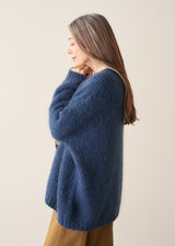 A woman wearing a blue chunky knit oversized cardigan with a checked shirt and mustard trousers