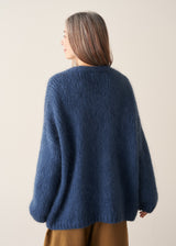 A woman wearing a blue chunky knit oversized cardigan with a checked shirt and mustard trousers