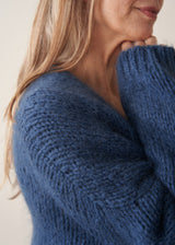 A woman wearing a blue chunky knit oversized cardigan with a checked shirt and mustard trousers