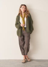 A woman wearing an oversized chunky knit sweater in khaki green with dark checked barrel leg trousers